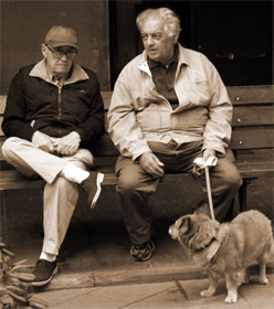 Two men sitting and talking, one with a dog on a leash
