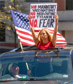 Woman holding sign: "No Mandatory Vaccinations, No Micro-Chipping, No Tyrrany, No Fear" next to American flag
