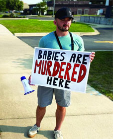 Man holding a sign, "Babies are murdered here"