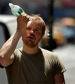 Overheated man holding plastic water bottle to his head