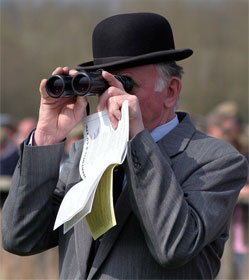 Man looking through binoculars and holding racing form