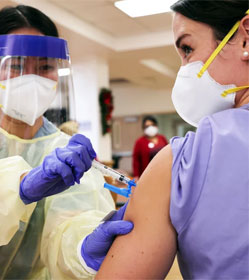 Woman in mask and face shield administering vaccine to woman in mask